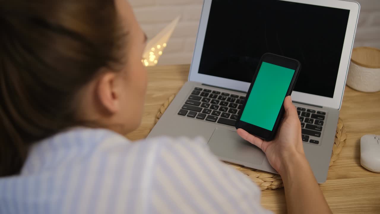 Green screen of the computer and phone. The girl is sitting at the table and browsing the Internet. The concept of distance learning. Rear view