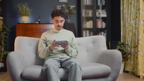 joven viendo una escena de película inesperada en un teléfono inteligente mientras se sienta en el sofá en casa 1