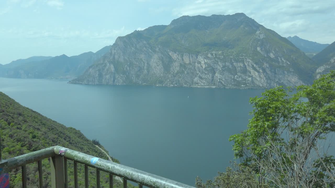 el sendero de barandillas de busatte del lago garda con barandillas metálicas contra un telón de fondo de cielo, agua, montaña y nubes