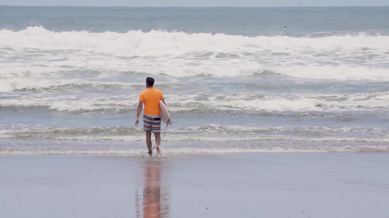 surfista con camisa naranja camina hasta la orilla en costa rica