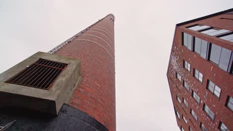 old factory chimney and a modern apartment house against a cloudy sky