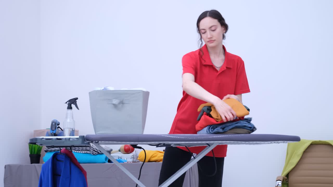 Una donna raccoglie il bucato pulito in un cesto sull'asse da stiro.