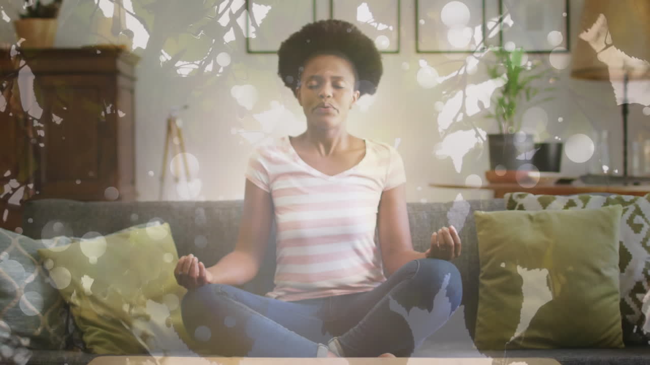 Animation of leaves and light spots over african american woman meditating, slow motion