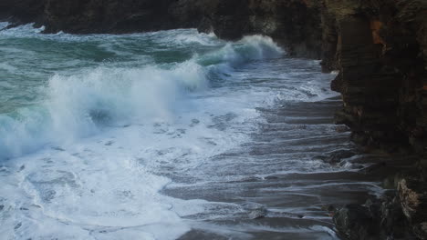 powerful foamy waves crashing on coastal cliffs at trevellas cove near st agnes, cornwall, england, uk - aerial static shot