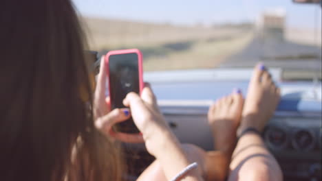 Hermosa-Chica-Tomando-Fotos-Con-Un-Teléfono-Inteligente-En-Un-Viaje-Por-Carretera-En-Un-Auto-Antiguo-Convertible