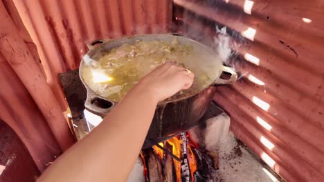 close-up of a traditional pot on a countryside fire in the dominican republic, cooking sancocho. steam rises as a metal spoon stirs the meats and vegetables in this authentic dish.