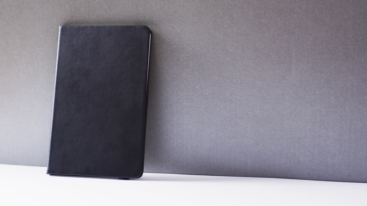 Close up of closed black book leaning on wall with copy space on gray background in slow motion