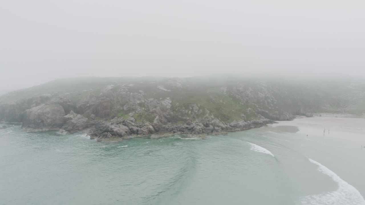 Drone shot of surfers, big waves and misty weather on Ceannabeinne Beach on the Scotland North Coast 500 Route which is the North Sea