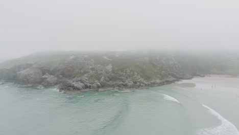drone shot of surfers, big waves and misty weather on ceannabeinne beach on the scotland north coast 500 route which is the north sea