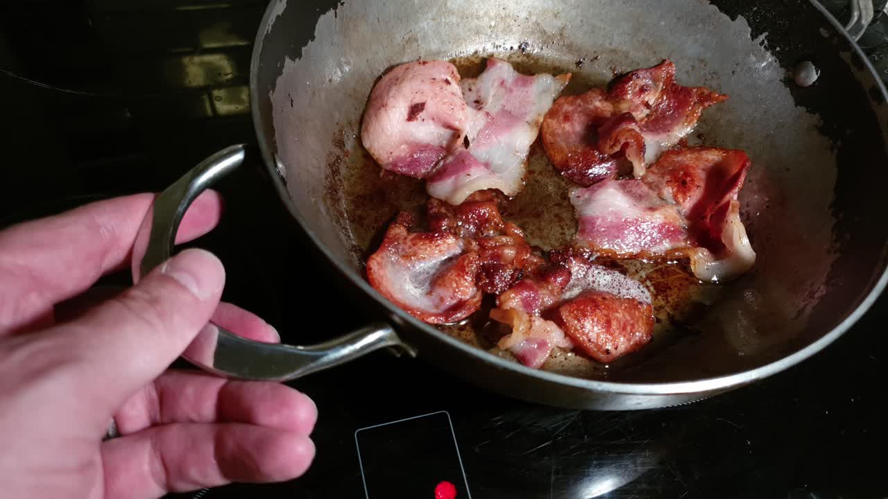 Sizzling back bacon strips frying in olive oil in a steel pan on glass stove top, perfect for morning breakfast