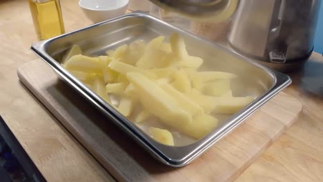 slow motion slider shot of emptying parboiled potatoes for fries into a metal baking tray