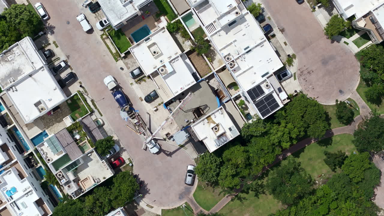 Zenith drone shot of a concrete pump pouring cement to make the tile of a house with several workers spreading the material
