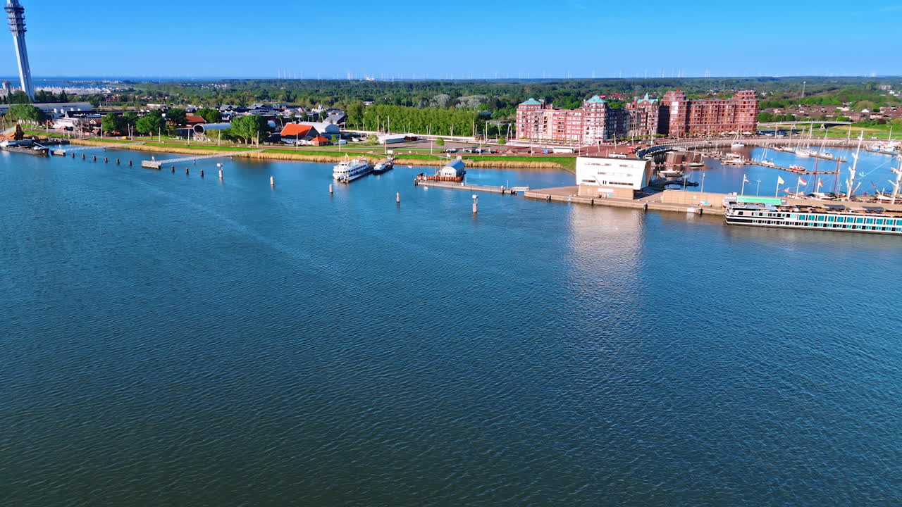 Footage above blue waterscape of the Markemeer lake. View on the port, green cityscape and telecom tower of Lelystad, the Netherlands.