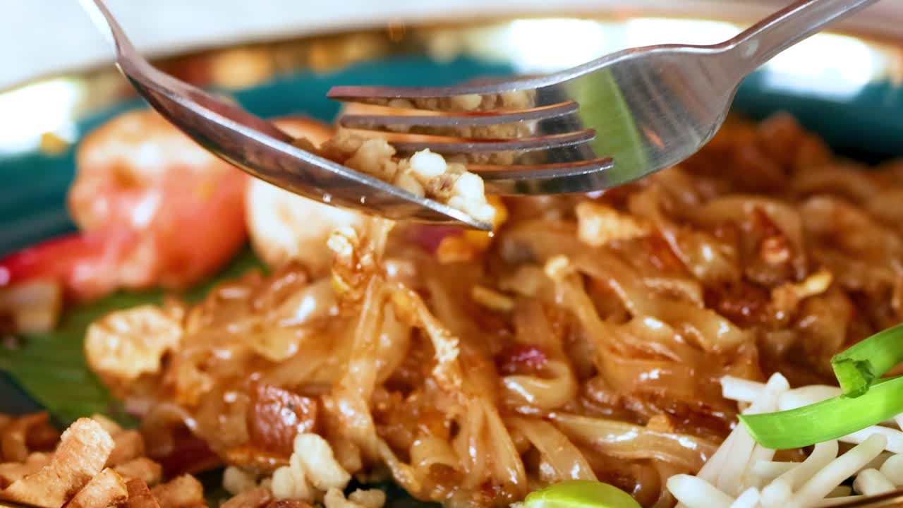 A detailed view of shrimp pad Thai with chopsticks and fork, highlighting ingredients and textures.