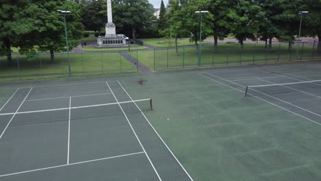 Aerial-view-flying-above-empty-council-park-fenced-tennis-court-and-skate-park