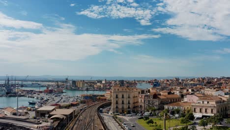 flying above railway with an aerial view of the sea port of catania with plane taking off in the background. industrial urban district in italy.