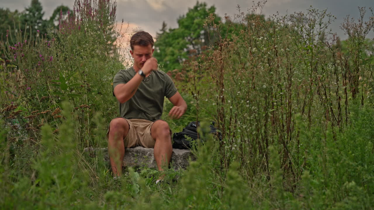A young man receives bad news on his phone and angrily throws it into his bag, expressing frustration, stress and emotional tension in a natural outdoor setting