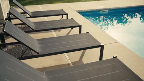 four black pool lounge chairs next to a pool during sunrise