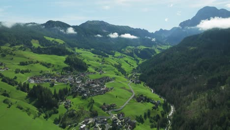 an aerial footage descends swiftly towards la val village, nestled amidst serene green hills, offering a stunning dolomites panorama in italy