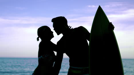 man with surfboard kissing girlfriend on the beach