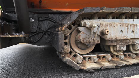 tracked paver laying asphalt - closeup of slowly rolling moving machine's tracks