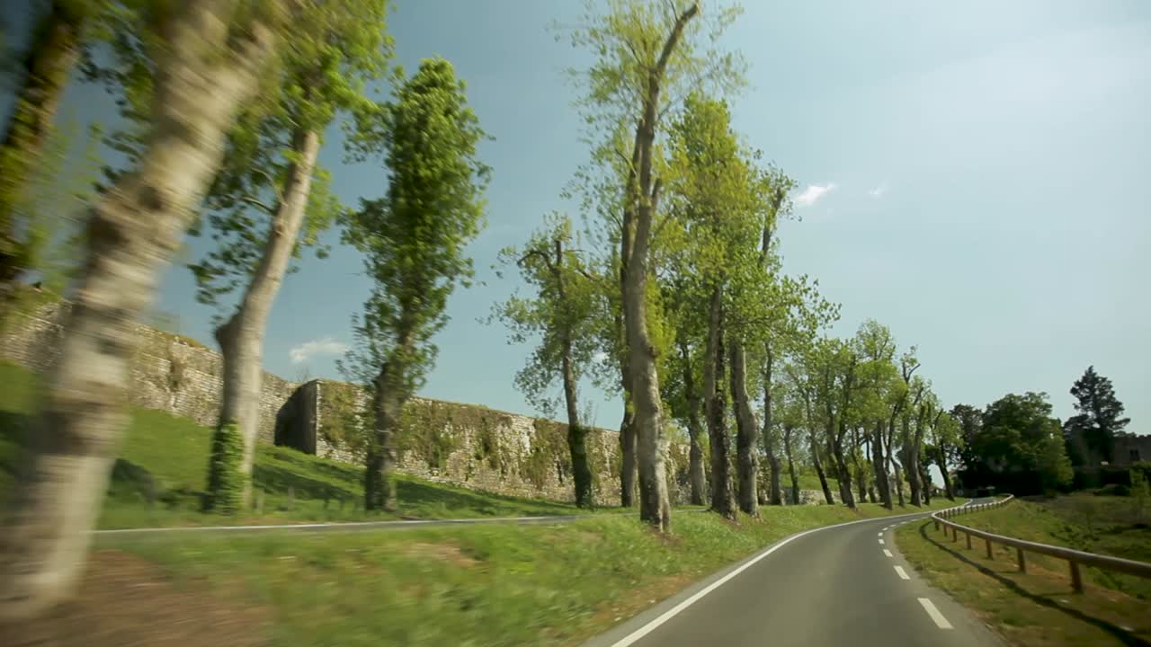 camino sinuoso en un entorno rural exuberante con árboles verdes y viejos muros de piedra, día soleado