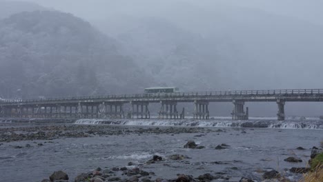 nieve cayendo sobre el puente togetsukyo en arashiyama mientras el autobús cruza