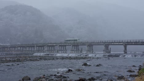 snow falling over togetsukyo bridge in arashiyama as bus crosses