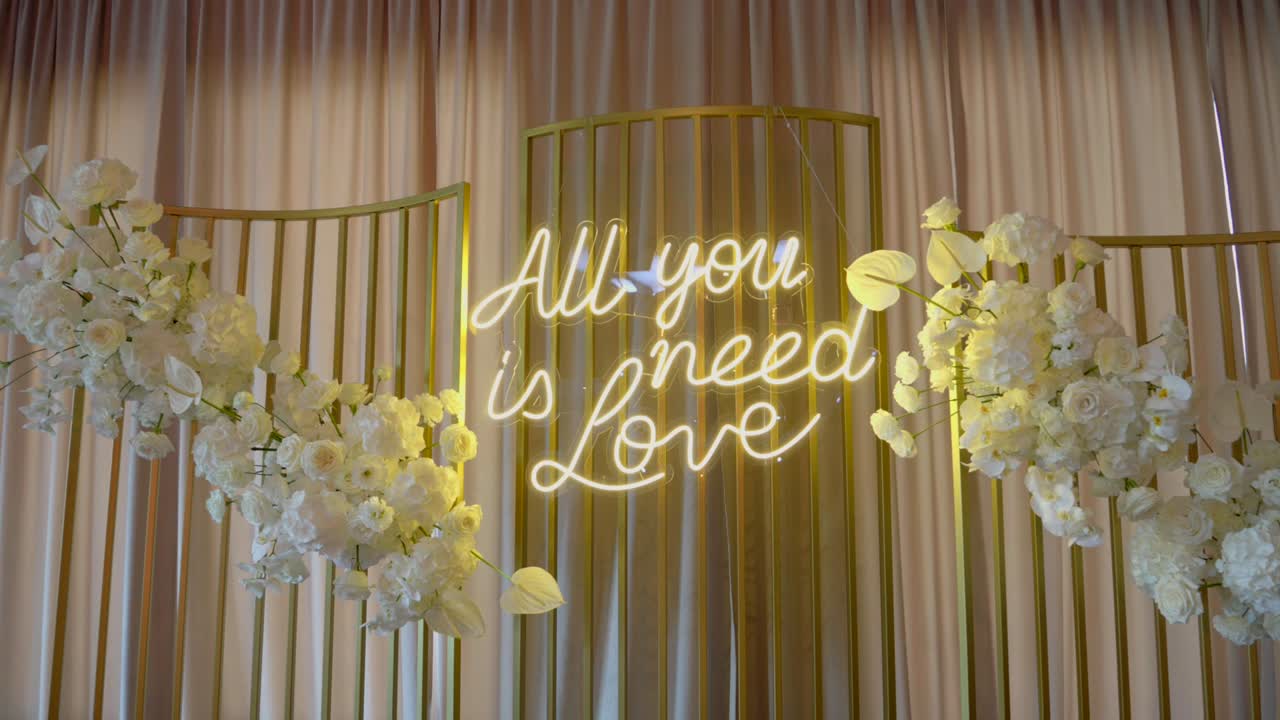 Insegna al neon con la scritta "All You Need Is Love" sulla parete di una sala per matrimoni