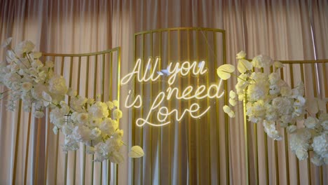 neon sign reading "all you need is love" on the wall in a wedding hall