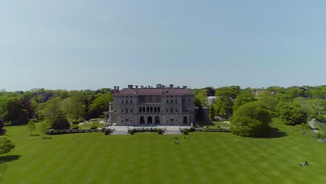 aerial of a large mansion house with a big yard on the coast near the ocean with tourists exploring nearby