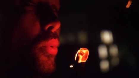 man blowing on heated ember with fire flakes flying. close up