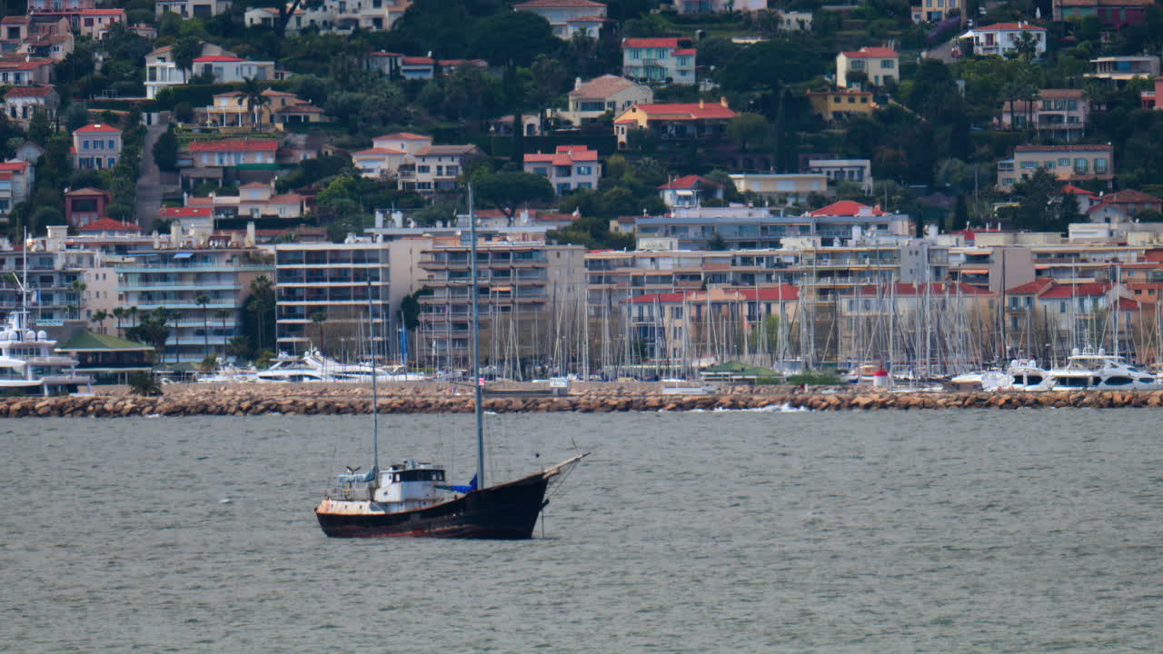 Rusty, white boat docked on the sea in Juan-les-Pins, France with the dock and the buildings on the background