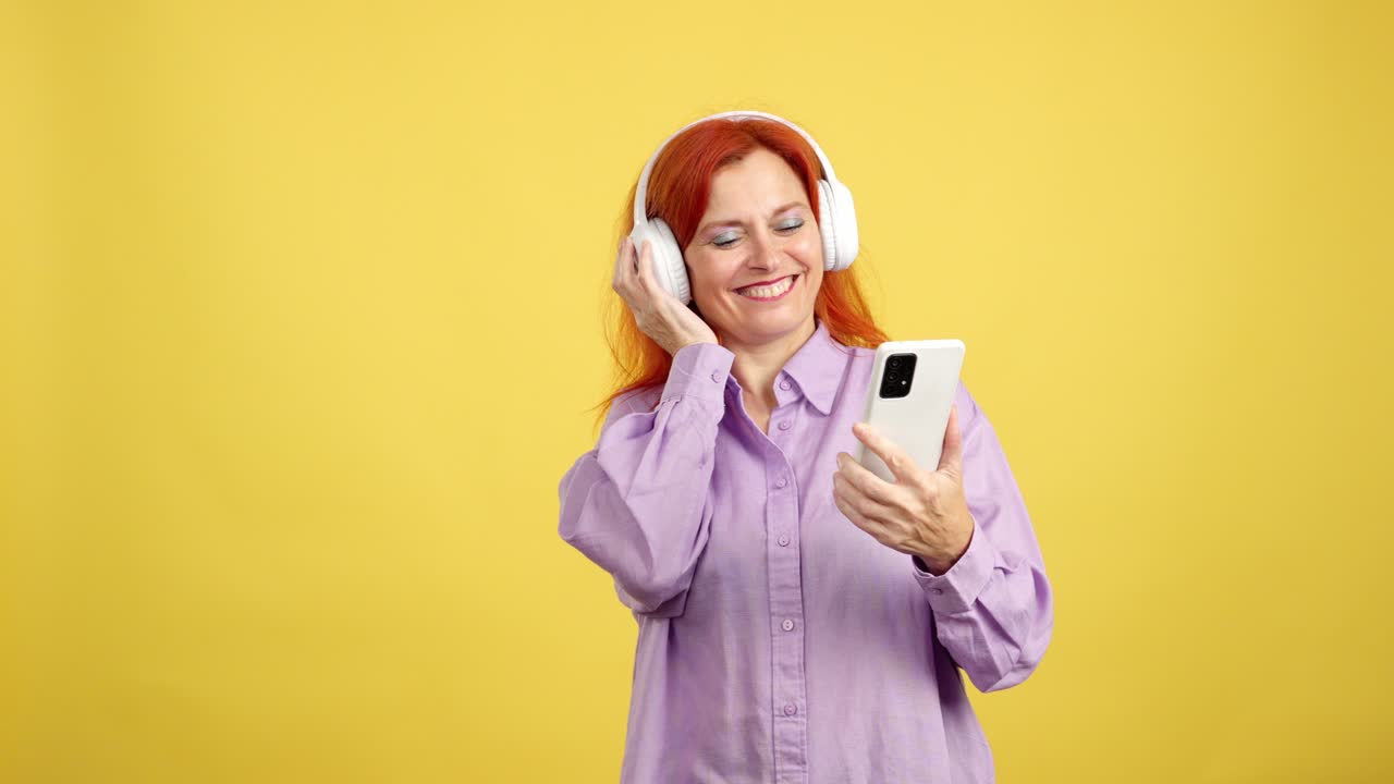 Happy red-haired woman listening to music with headphones and using a smartphone