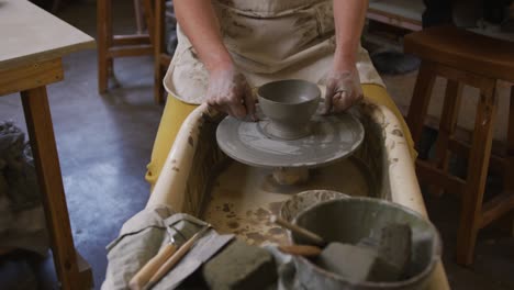 mid section of female potter using loop tool for finishing pottery at pottery studio