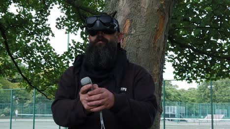 hombre barbudo usando gafas de realidad virtual fpv controlando drones en el parque con joystick de movimiento