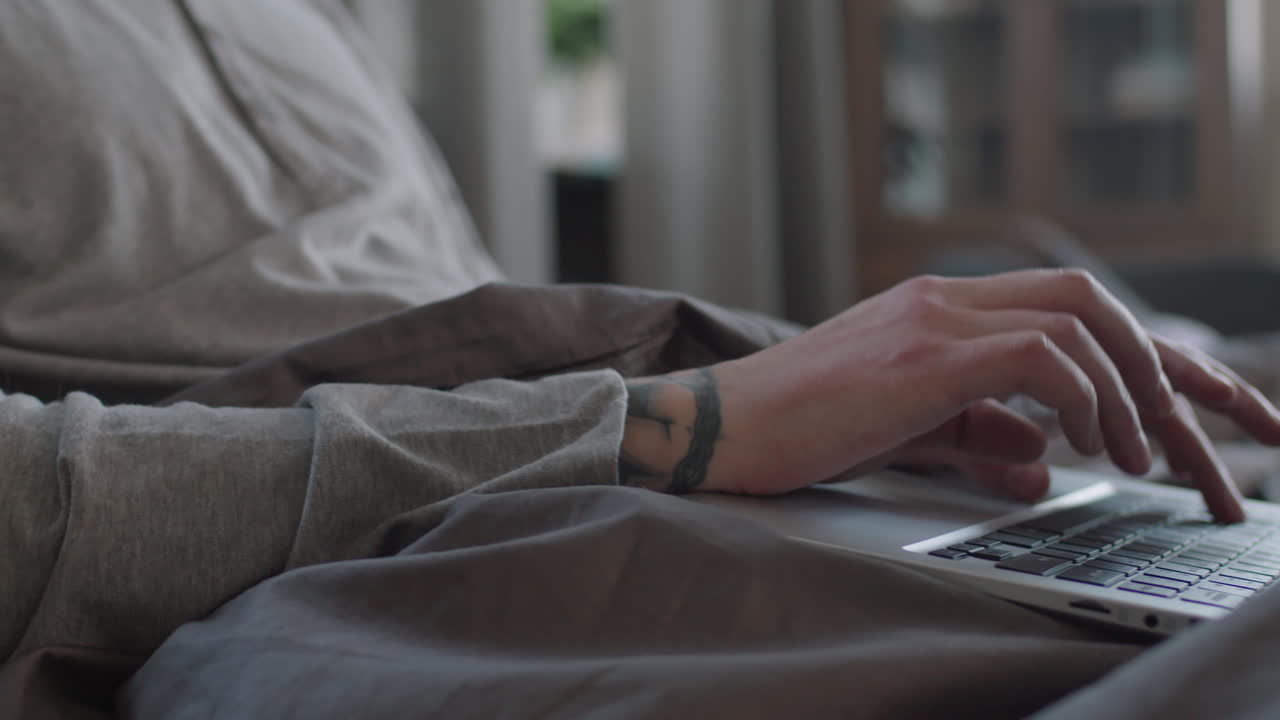 Man Typing On Laptop While Sitting In Bed