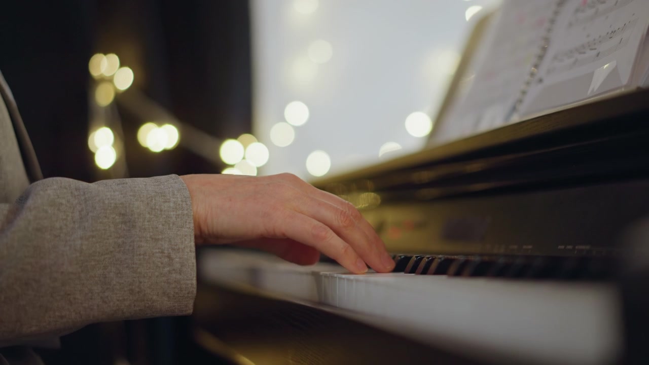 Mani suonano il pianoforte. Esercitazione riservata con luci calde. Musicista concentrato che si esercita da solo in un'atmosfera interna accogliente. Primo piano delle dita sui tasti con illuminazione delicata e spartito musicale nelle vicinanze