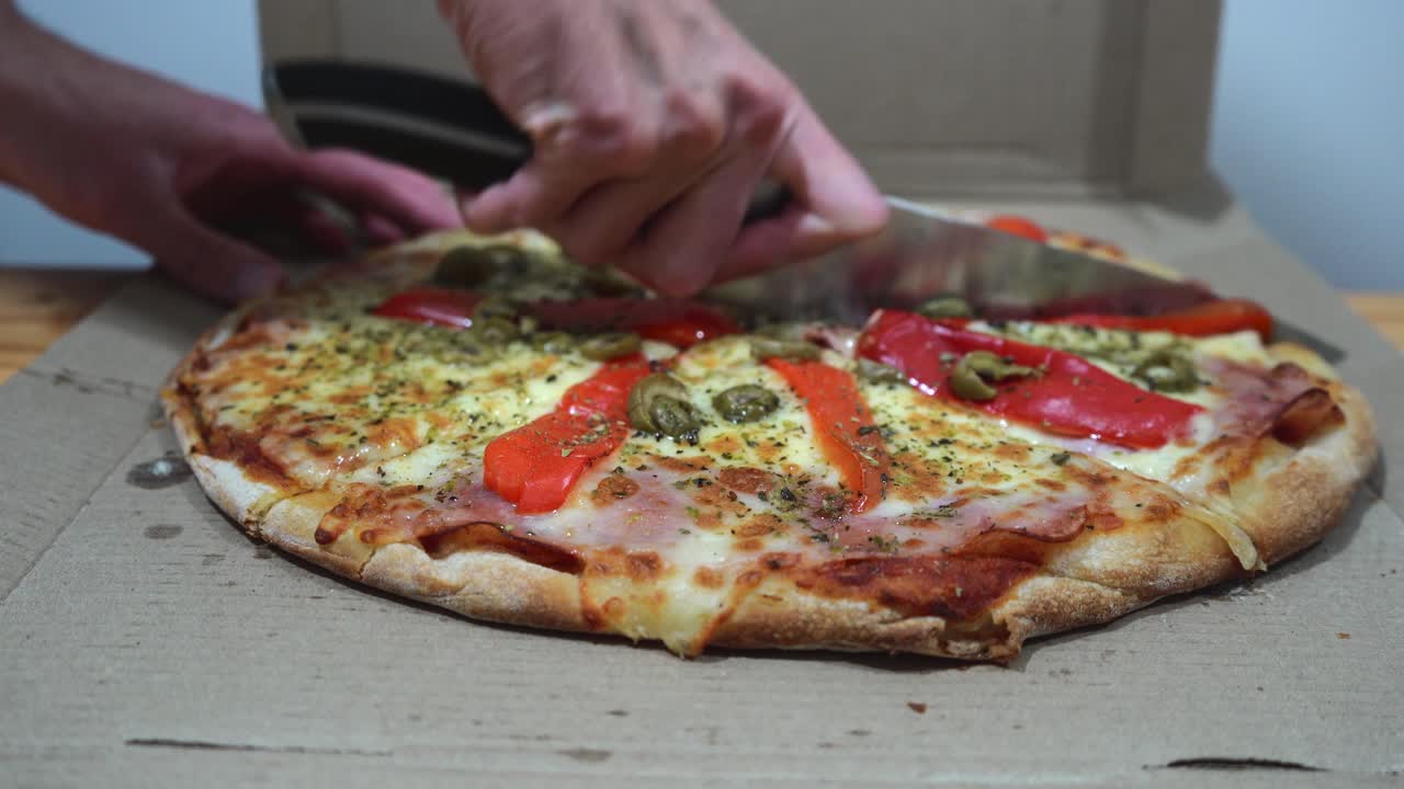 мужские руки разрезают вкусную пиццу на кусочки ножом внутри коробки