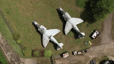 Aerial-Birdseye-view-circling-two-military-Sea-Harrier-jets-on-grassy-Charlwood-logistics-yard,-Surrey