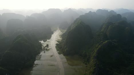 Sampan-Boat-Tours-on-Ngo-Dong-River-Weaving-in-Striking-Limestone-Karsts-Valley-on-Foggy-Sunset-in-Ninh-Binh-Vietnam---Aerial-orbit-view