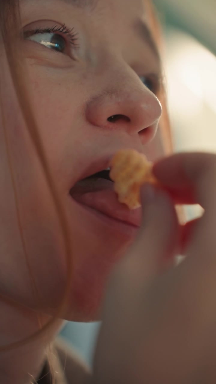 Close up of young woman face with light colored. Hand partially obscures frame in some segments while another woman is visible nearby. Sequence includes eating with woman