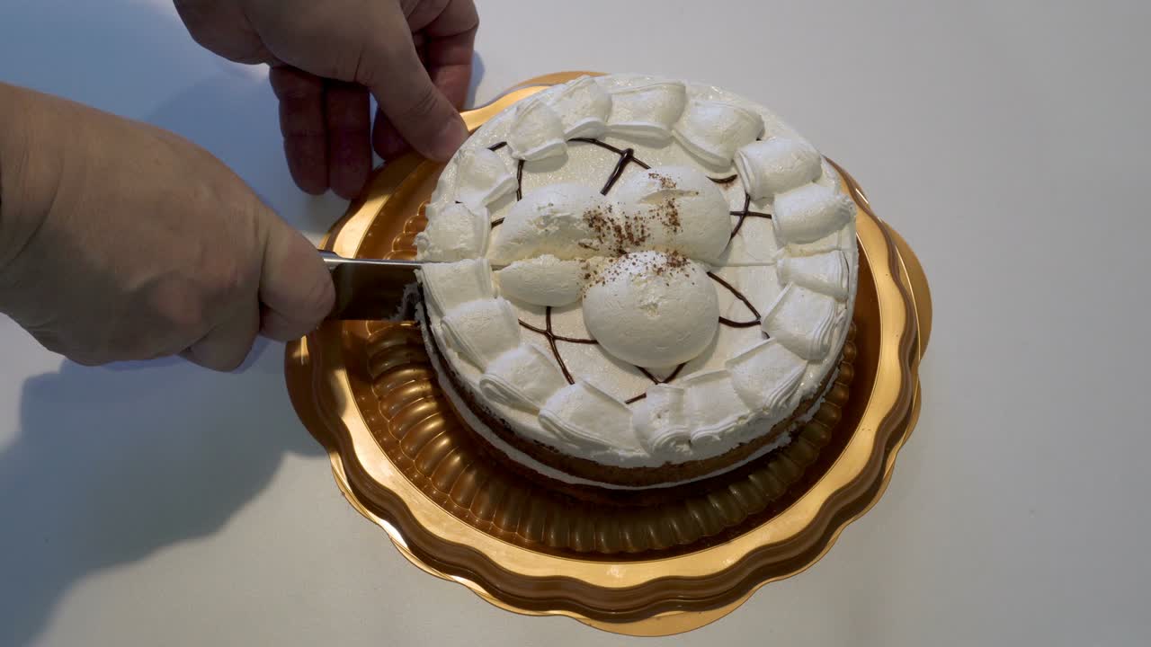 Un uomo adulto taglia una torta alla crema bianca su un piatto giallo con un grande coltello da cucina. Il concetto della festa. Primo piano. Senza volto. Vista dall'alto. 4K