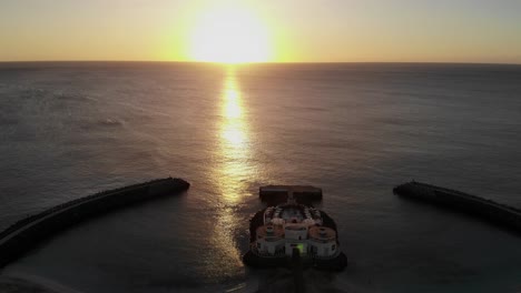 Vista-Aérea-De-La-Puesta-De-Sol-Amarilla-Dorada-Sobre-El-Océano-En-El-Horizonte-Con-Vista-De-Silueta-Club-De-Playa-Bikini