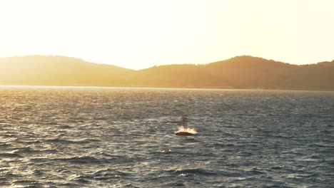 Buoy-floating-on-the-waters-of-the-Ionian-Sea-in-the-rays-of-the-setting-sun,-against-the-backdrop-of-Greek-islands