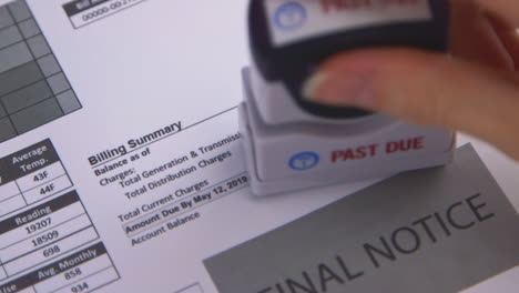 A slow motion close up pan of a woman&#039;s hand stamping &amp;quot;Past Due&amp;quot; on some bills