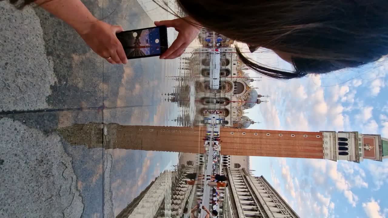 toma vertical de una creadora de contenido femenina filmando, fotografiando el campanile, venecia
