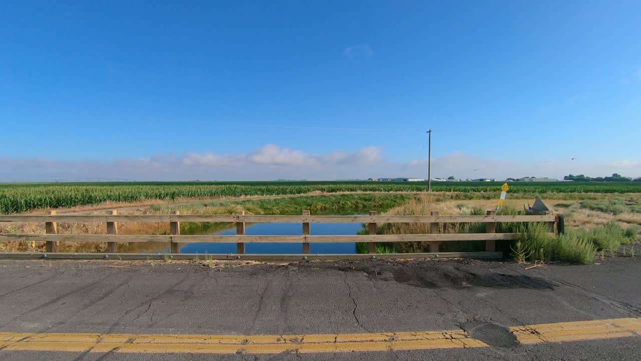 Pan of bridge over an irrigation canal; Visible are a corn field in the background