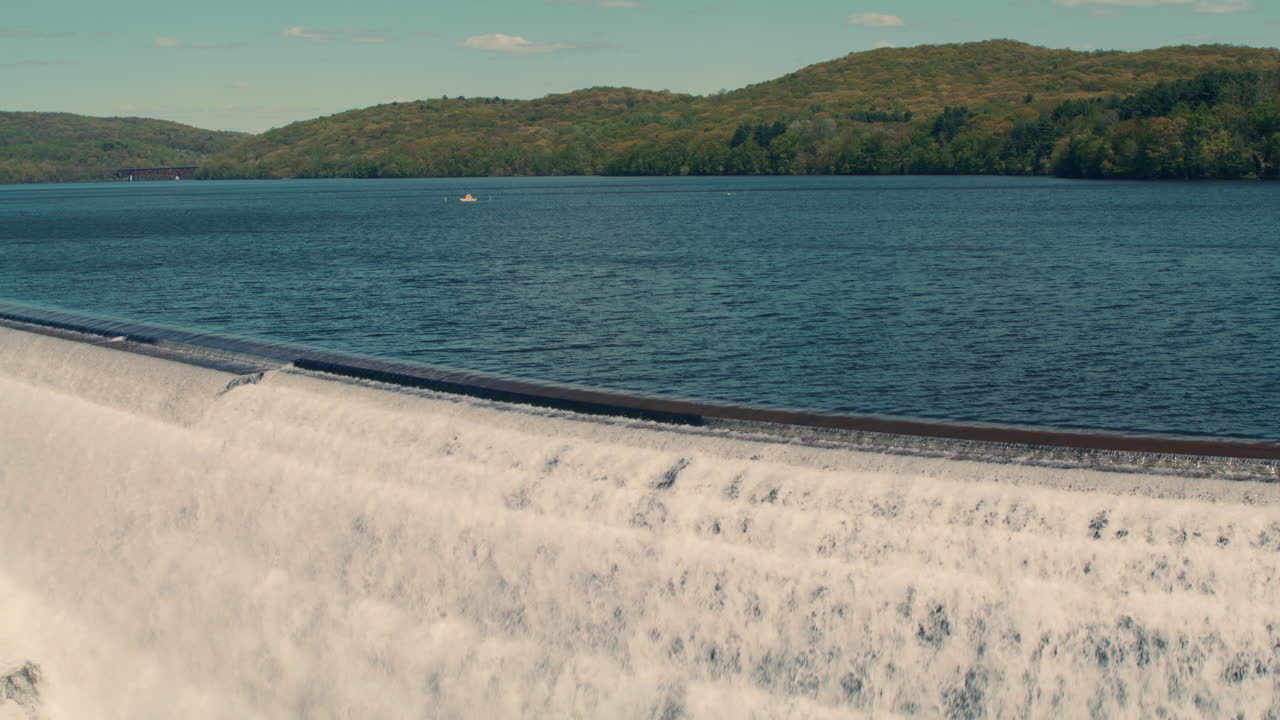 medium shot of new croton reservoir stepped spillway with lake, mountains and blue sky in the background. slow motion 40fps