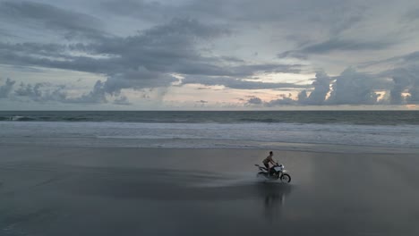 man rides motorccle on sandy ocean beach in cloudy morning light